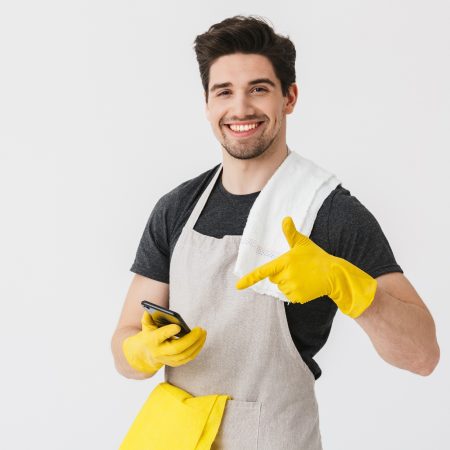 Handsome brunette houseman wearing apron standing isolated over white background, showing mobile phone